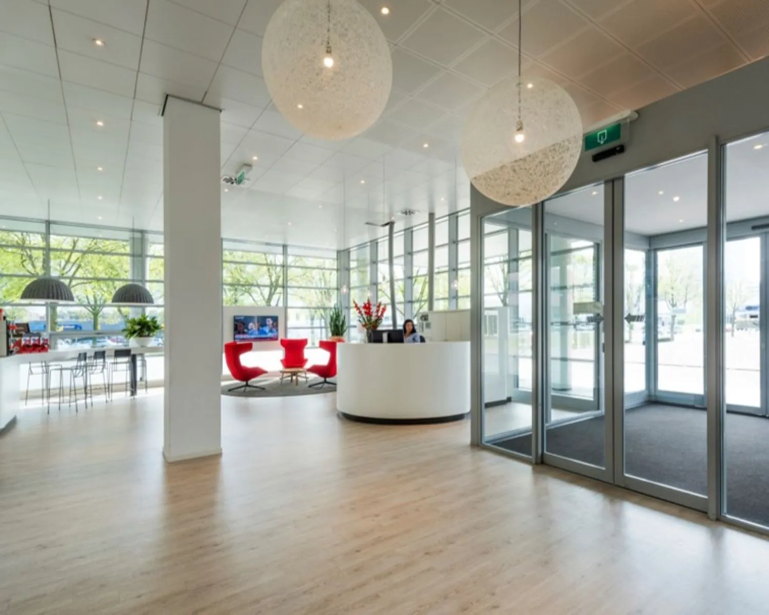 Moderne en lichte ontvangsthal met glazen schuifdeuren, een receptiebalie en rode loungefauteuils.