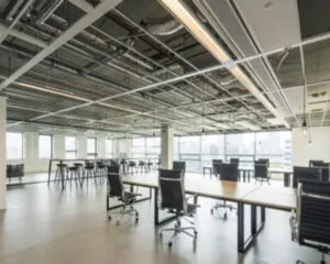 Moderne, open kantoorruimte met bureaus, zwarte bureaustoelen en industriële plafonds.