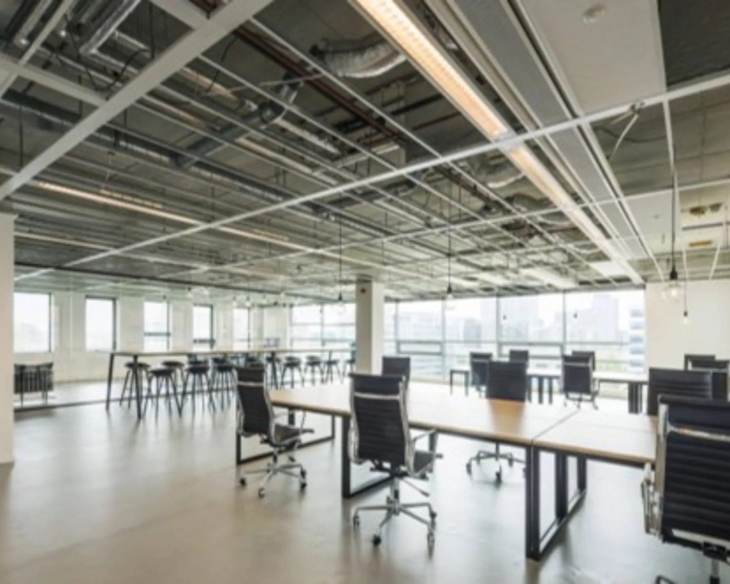 Moderne, open kantoorruimte met bureaus, zwarte bureaustoelen en industriële plafonds.