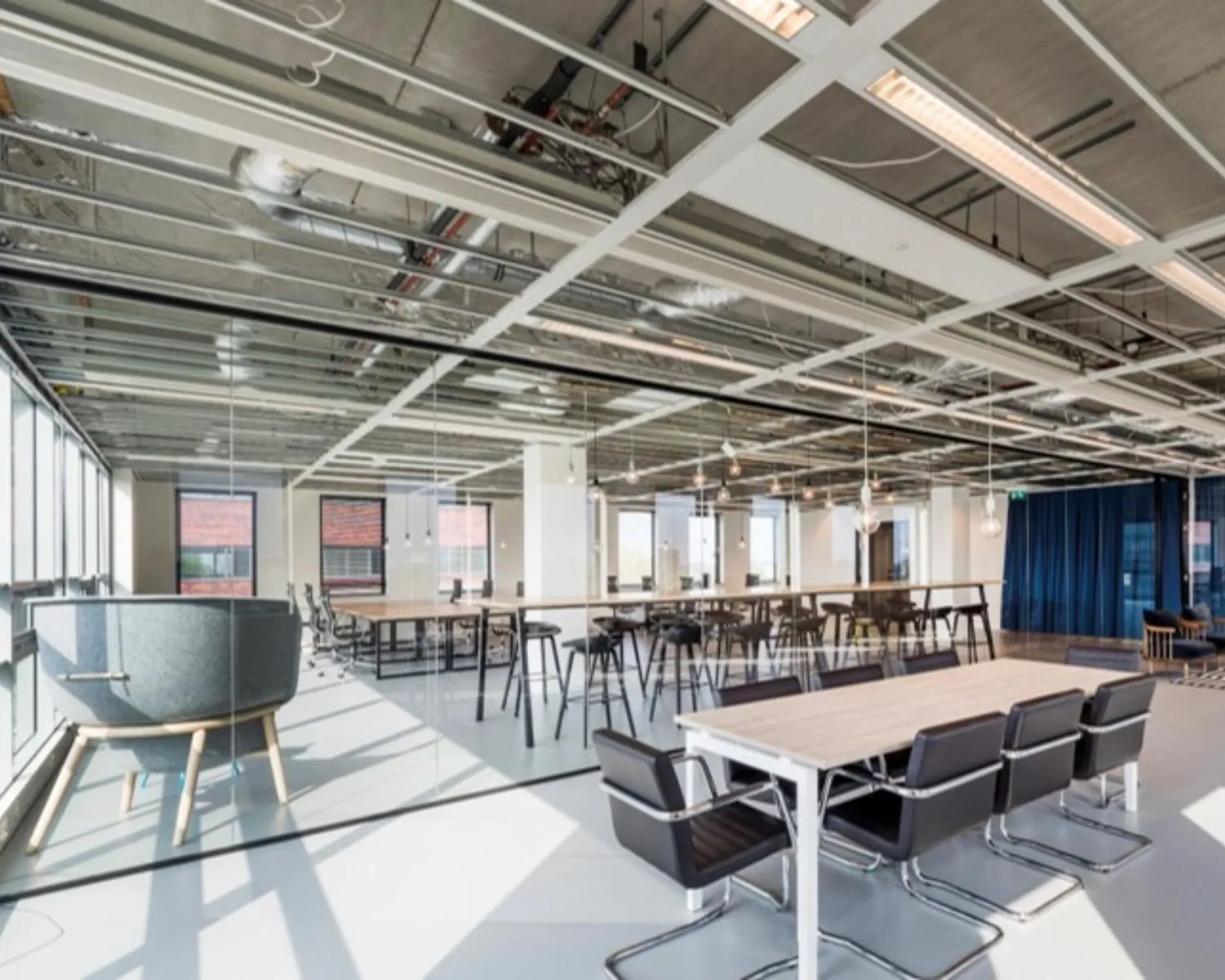 Moderne, open kantoorruimte met glazen wanden, industriële plafonds en verschillende zit- en werkplekken.