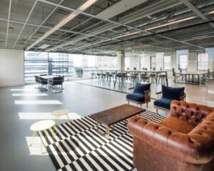 Modern ingerichte kantooruimte met een leren bank, loungehoek en grote ramen met uitzicht op de stad.