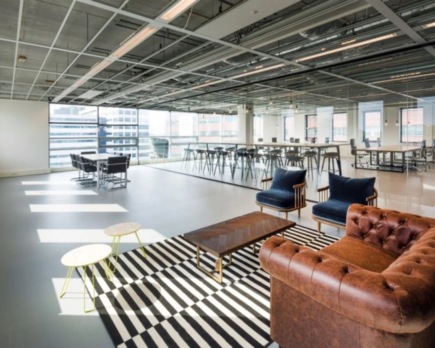 Modern ingerichte kantooruimte met een leren bank, loungehoek en grote ramen met uitzicht op de stad.