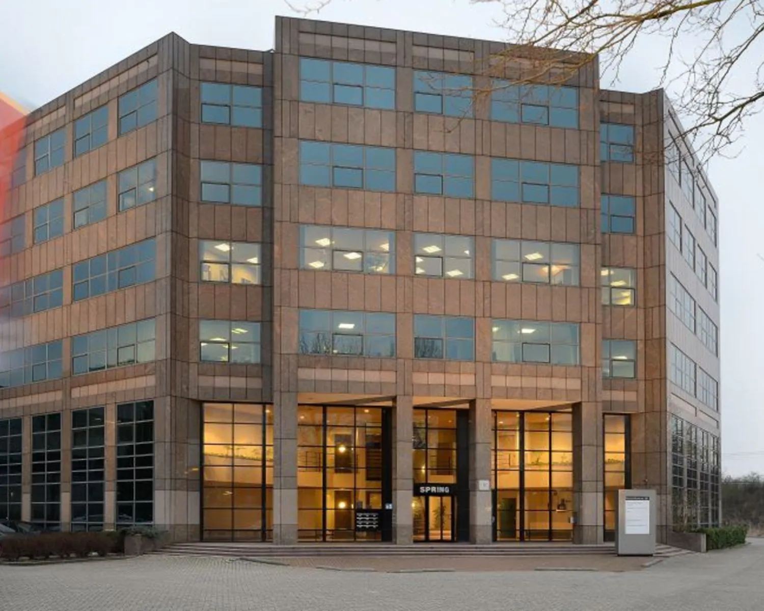 Een modern kantoorgebouw met grote ramen en de naam "SPRING" boven de ingang.
