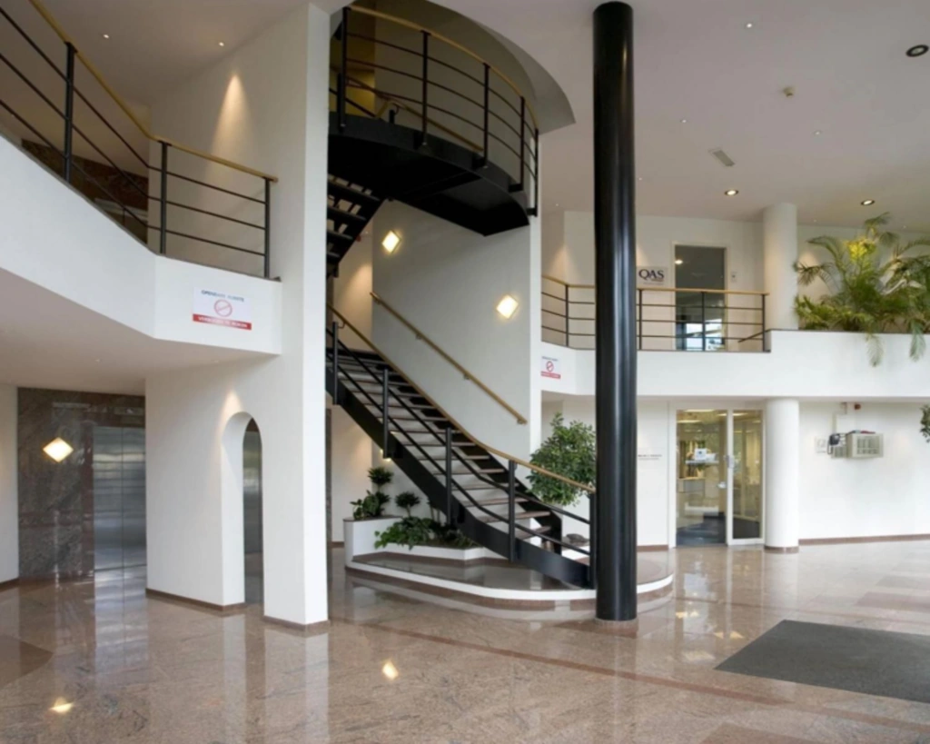 Moderne kantoorentree met een zwarte wenteltrap, glanzende marmeren vloer en glazen deuren.