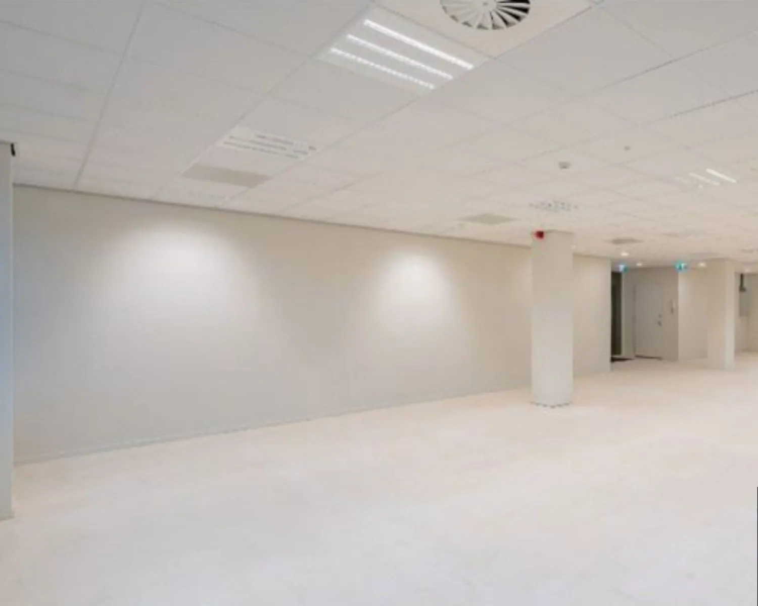 Leeg, wit en modern kantoor- of bedrijfsruimte-interieur met systeemplafond en pilaren.
