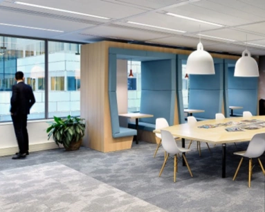 Moderne kantoorlounge met zithoeken, grote vergadertafel en een man die uit het raam kijkt.