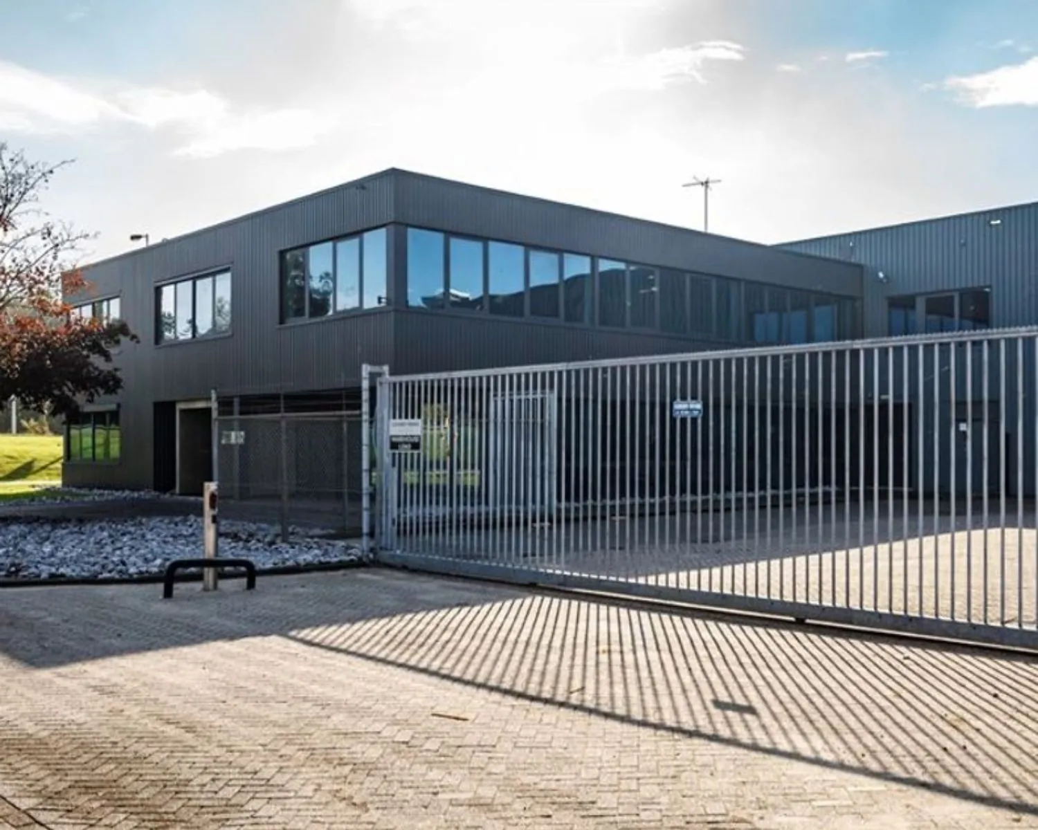 Modern bedrijfsgebouw met donkere gevelbekleding achter een gesloten metalen schuifpoort.