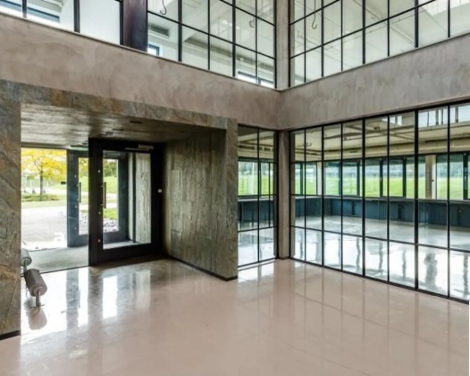 Moderne, lichte entreehal met glazen wanden en glanzende vloer in een kantoorgebouw.