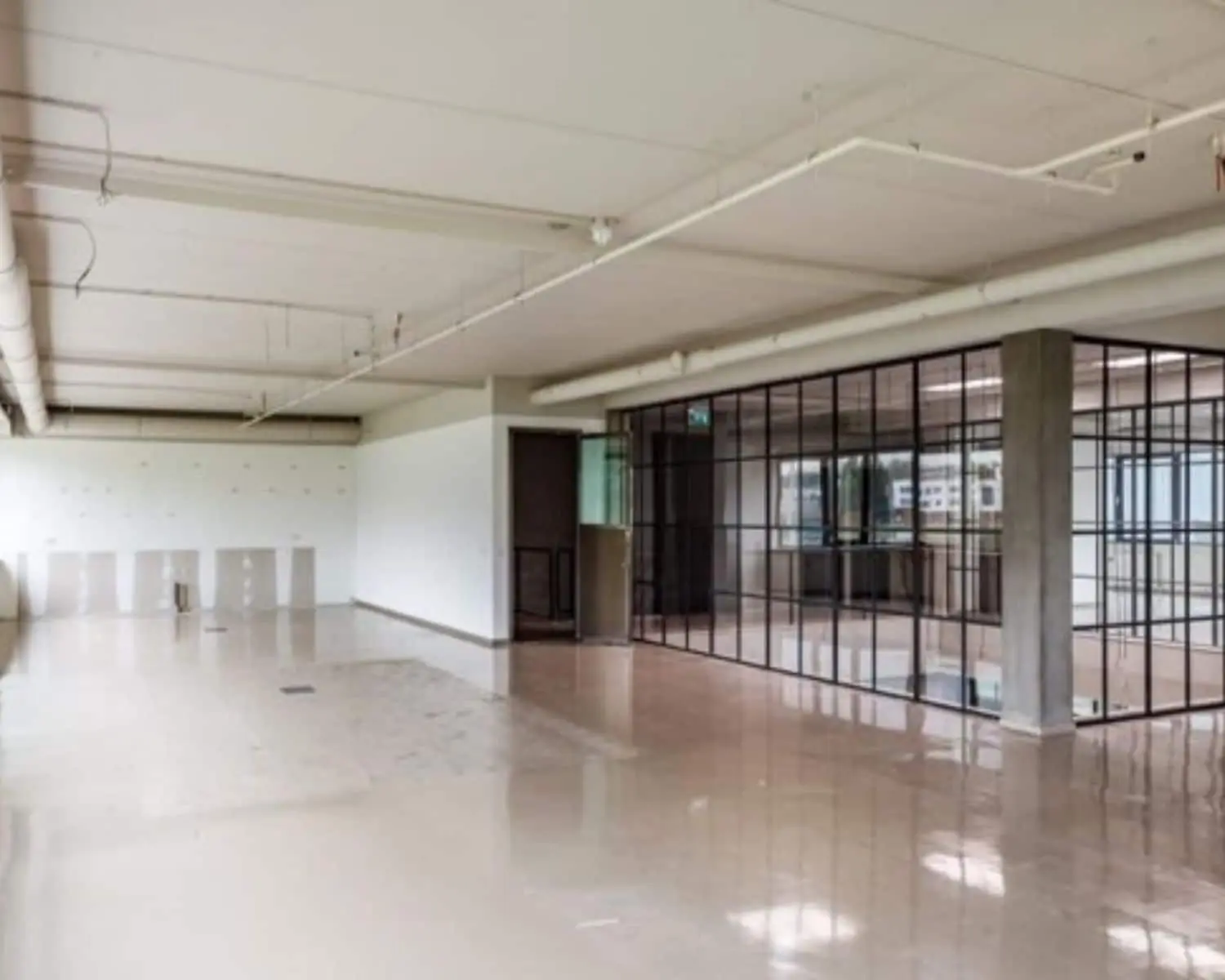 Leegstaand kantoorpand met glazenschuifwanden en betonnen vloer.