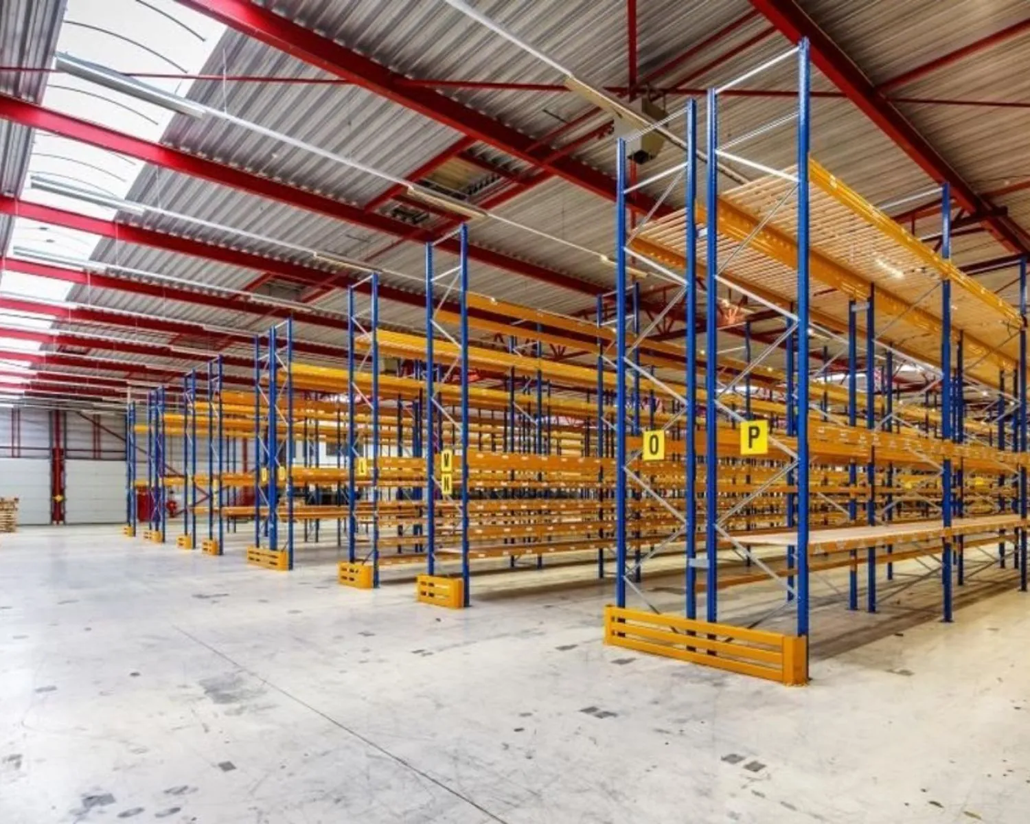 Lege magazijnhal met hoge, metalen opslagstellingen en betonnen vloer.