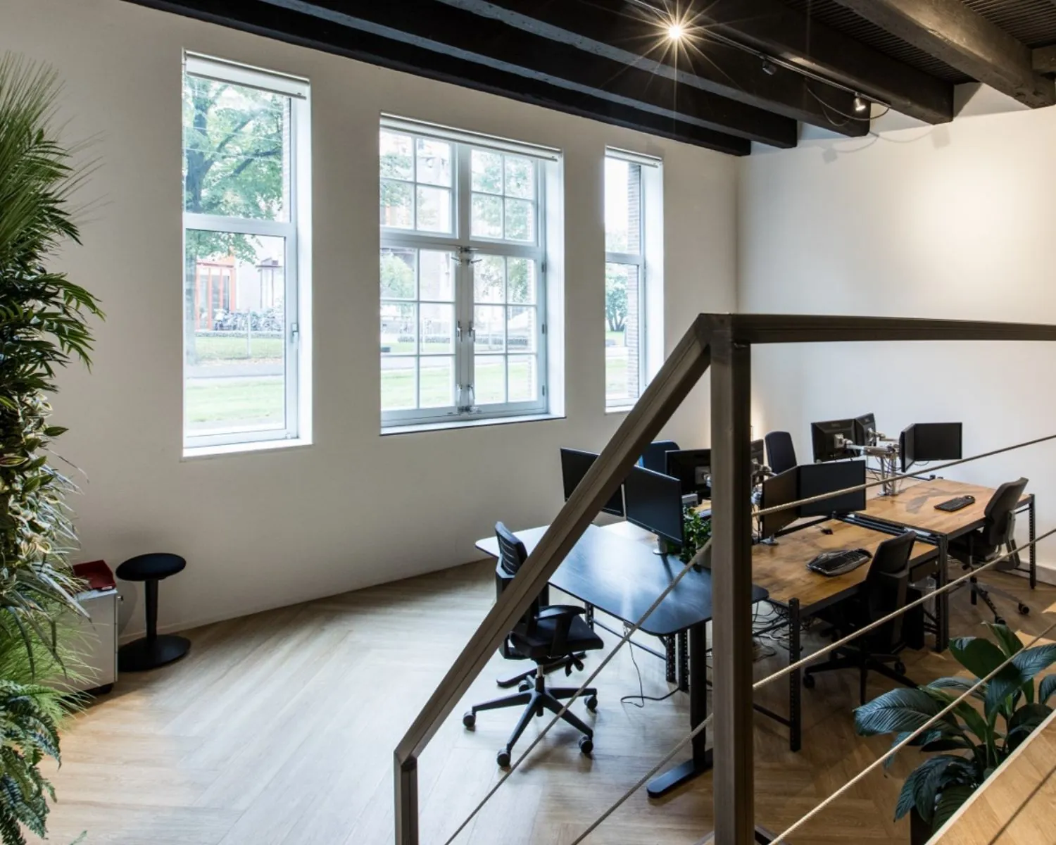 Moderne en lichte kantoorruimte met meerdere bureaus, computerschermen en grote ramen.