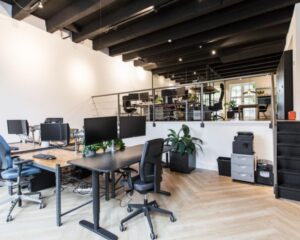 Moderne open kantoorruimte met bureaus, computers en een tussenverdieping met extra werkplekken.