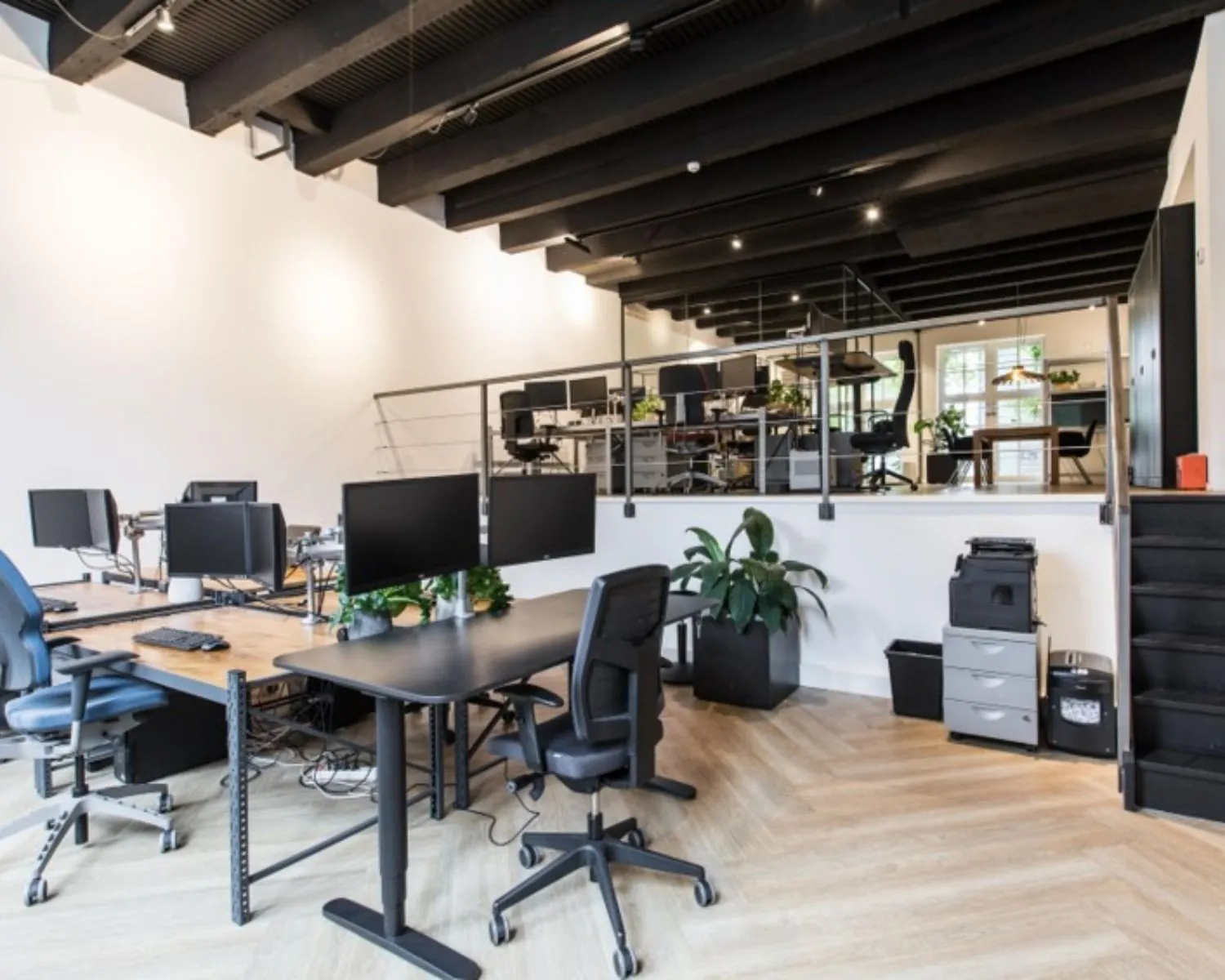 Moderne open kantoorruimte met bureaus, computers en een tussenverdieping met extra werkplekken.