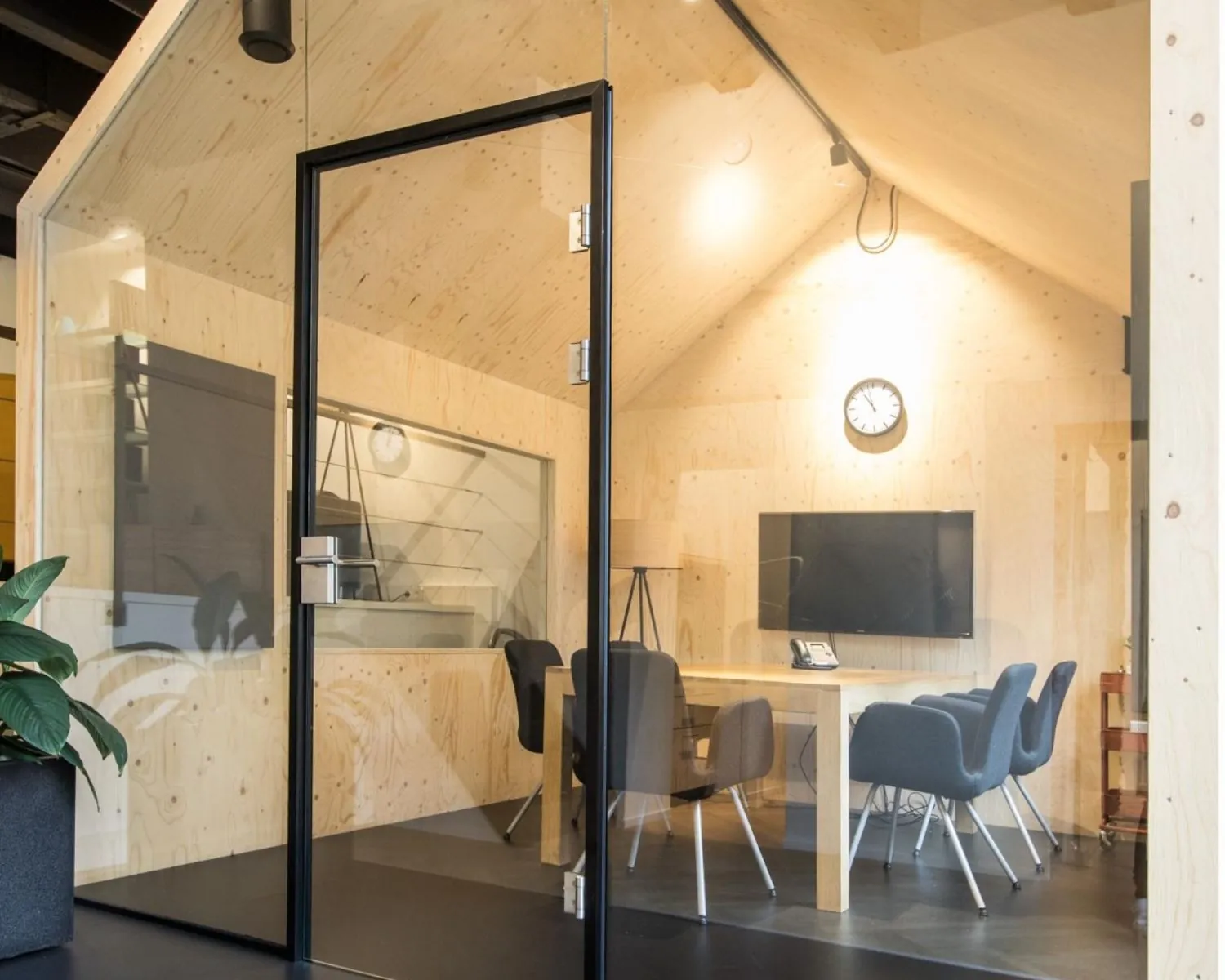 Vergaderruimte in de vorm van een houten cabine met glazen wanden, vergadertafel, stoelen, klok en een flatscreen-tv.