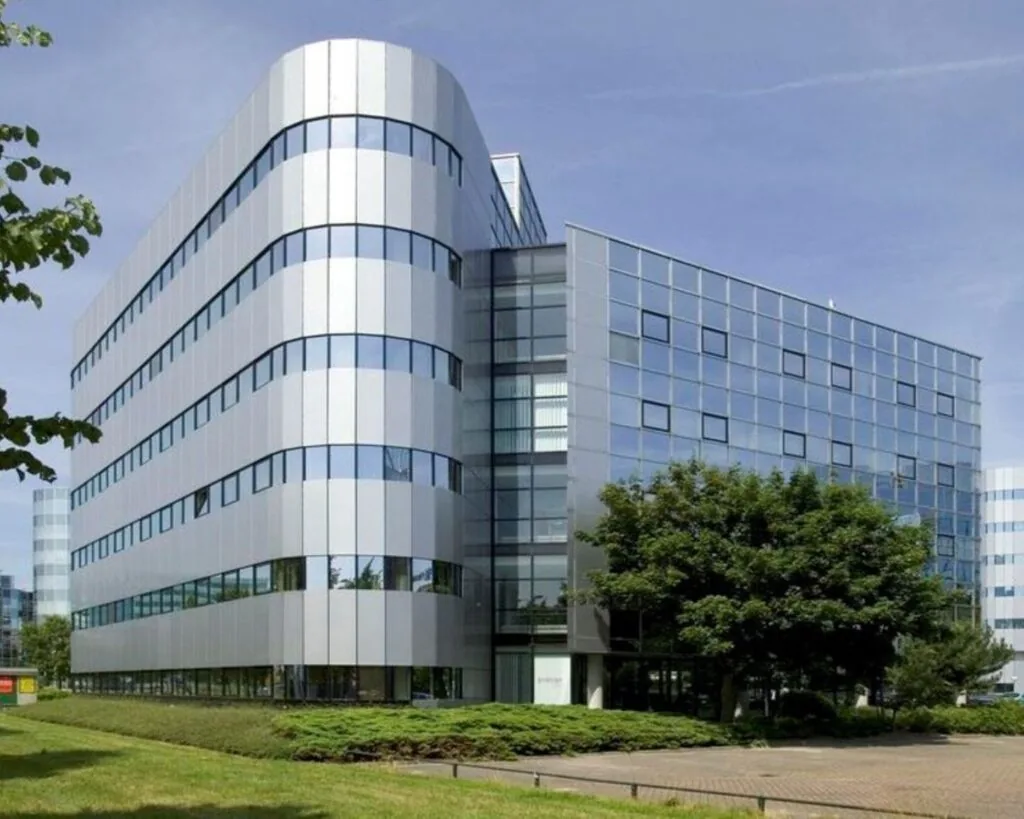 Modern kantoorgebouw met glazen en metalen gevels omgeven door groen en bestrating.