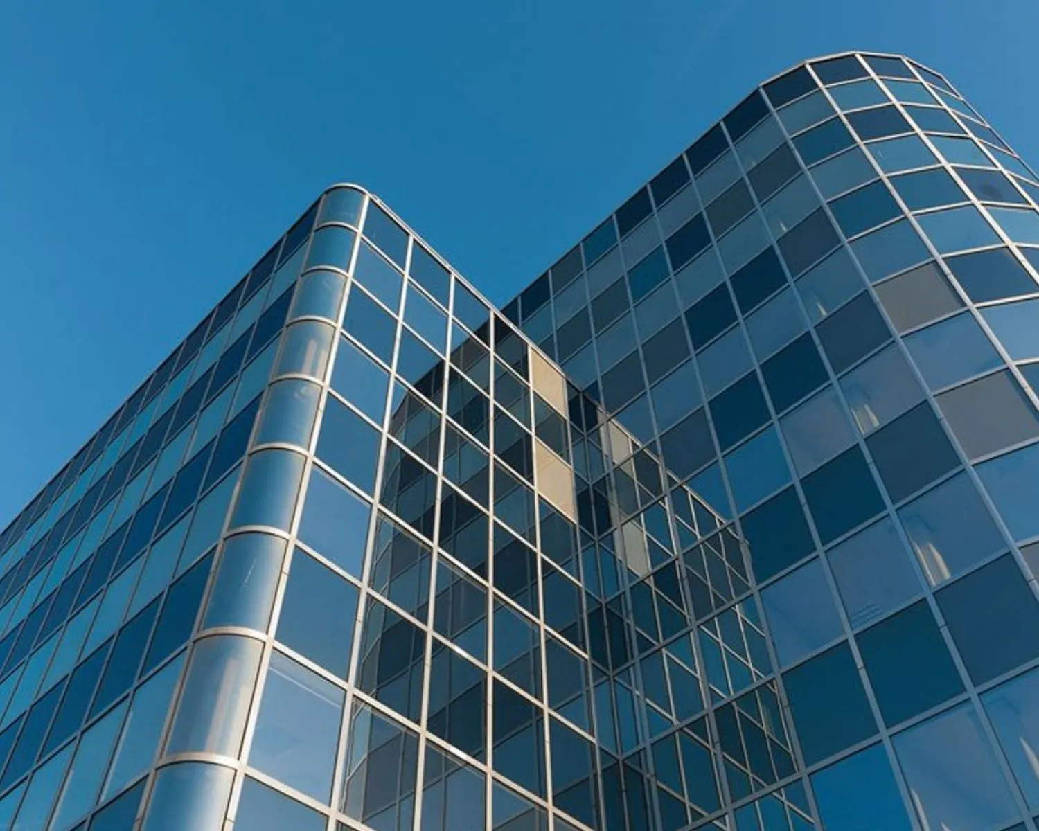 Modern kantoorgebouw met een glazen gevel tegen een heldere blauwe lucht.