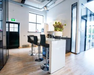 Moderne kantoorkeuken met hoge stoelen, een wit kookeiland en grote ramen.