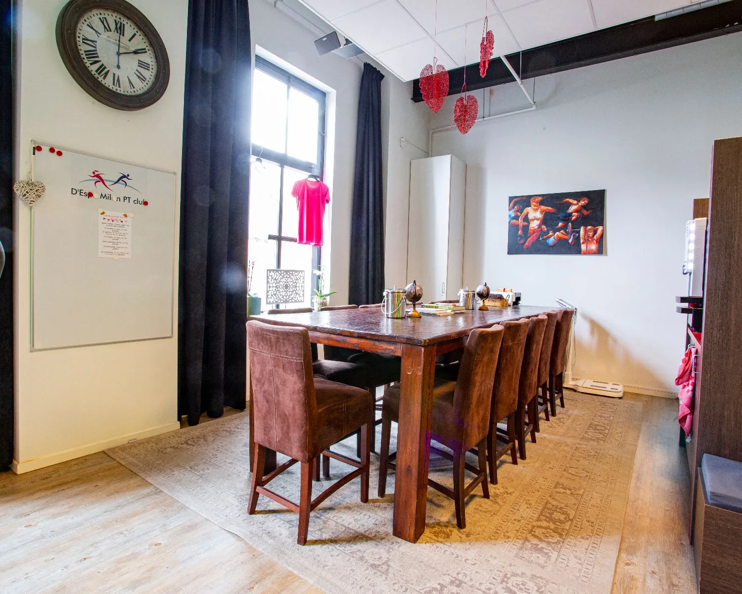 Vergaderruimte met een lange houten tafel, bruine stoelen, decoratieve harten aan het plafond en een schilderij aan de muur.