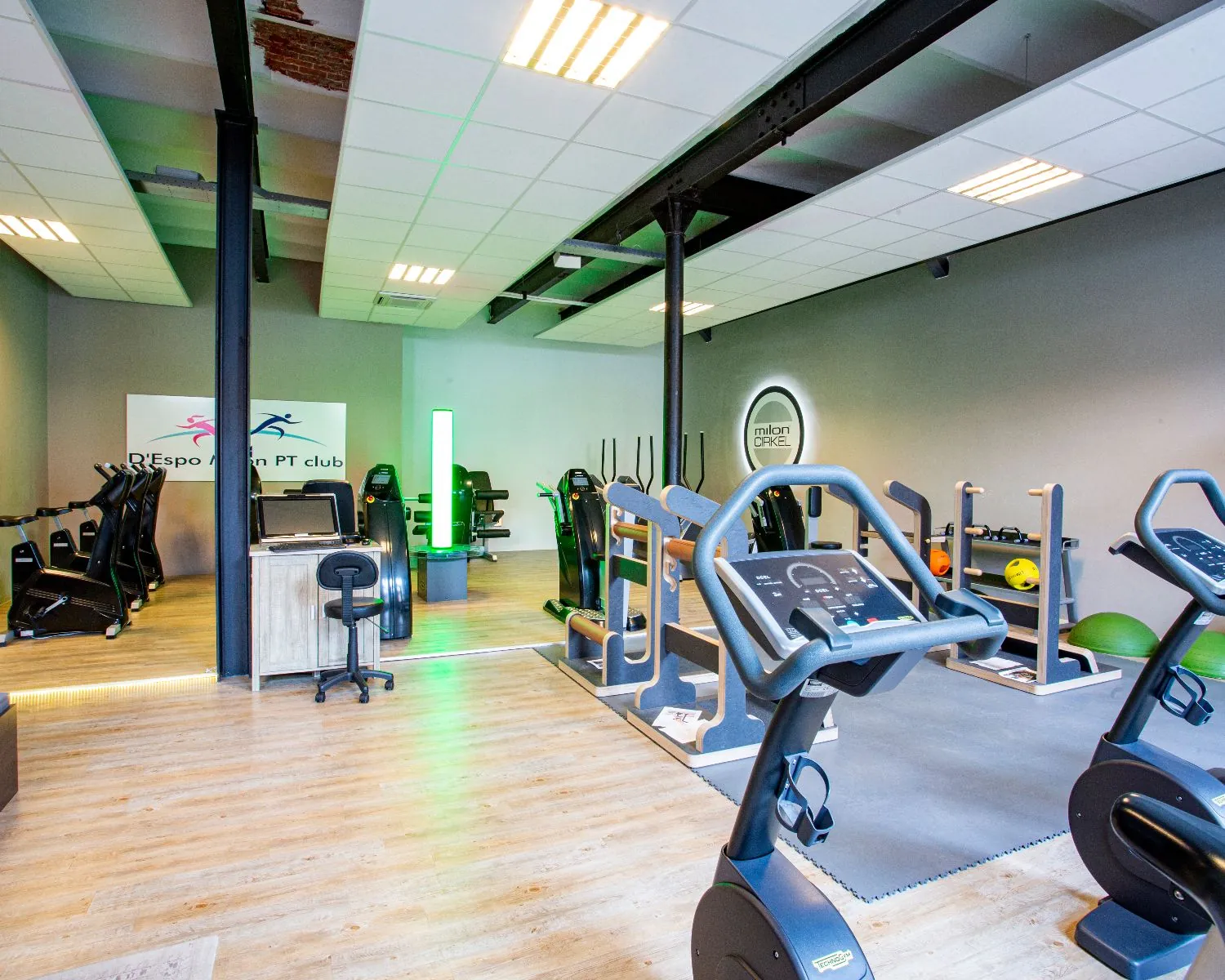Moderne fitnessruimte met diverse cardio- en krachttoestellen en een ontvangstbalie in het midden.