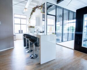 Moderne, lichte keukenruimte met witte wanden, zwarte barkrukken en glazen wanden.