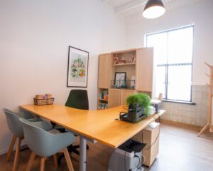 Licht en modern kantoor met houten meubels, planten en een grote raamopening.