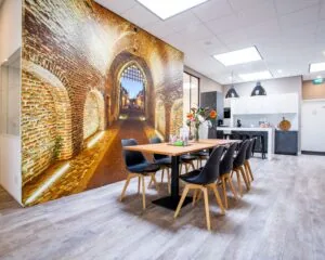 Moderne kantine met een grote fotowand van een verlichte middeleeuwse stadspoort, houten eettafel en open keuken.