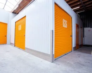 Een gang met meerdere oranje opslagunits met opgerolde deuren in een lichte, overdekte loods.
