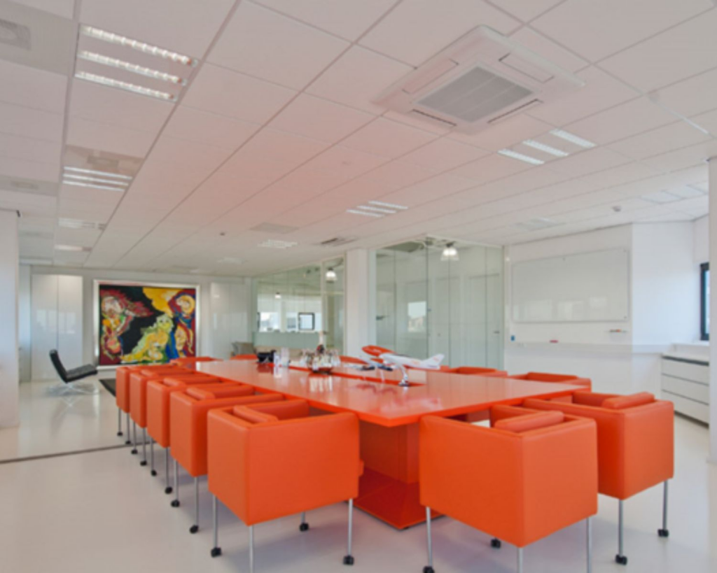 Moderne vergaderruimte met feloranje stoelen en tafel, omringd door glazen wanden en kleurrijke kunst aan de muur.