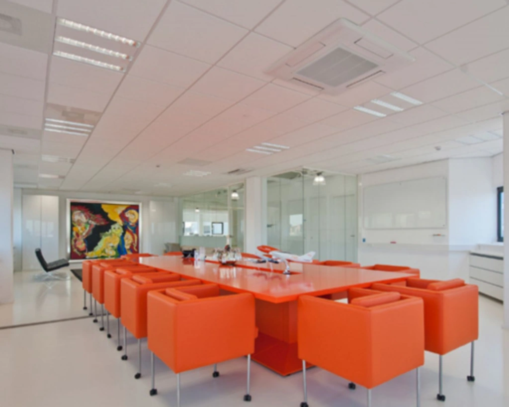 Moderne vergaderruimte met feloranje stoelen en tafel, omringd door glazen wanden en kleurrijke kunst aan de muur.