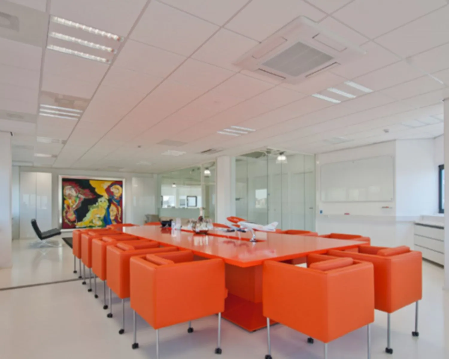 Moderne vergaderruimte met feloranje stoelen en tafel, omringd door glazen wanden en kleurrijke kunst aan de muur.