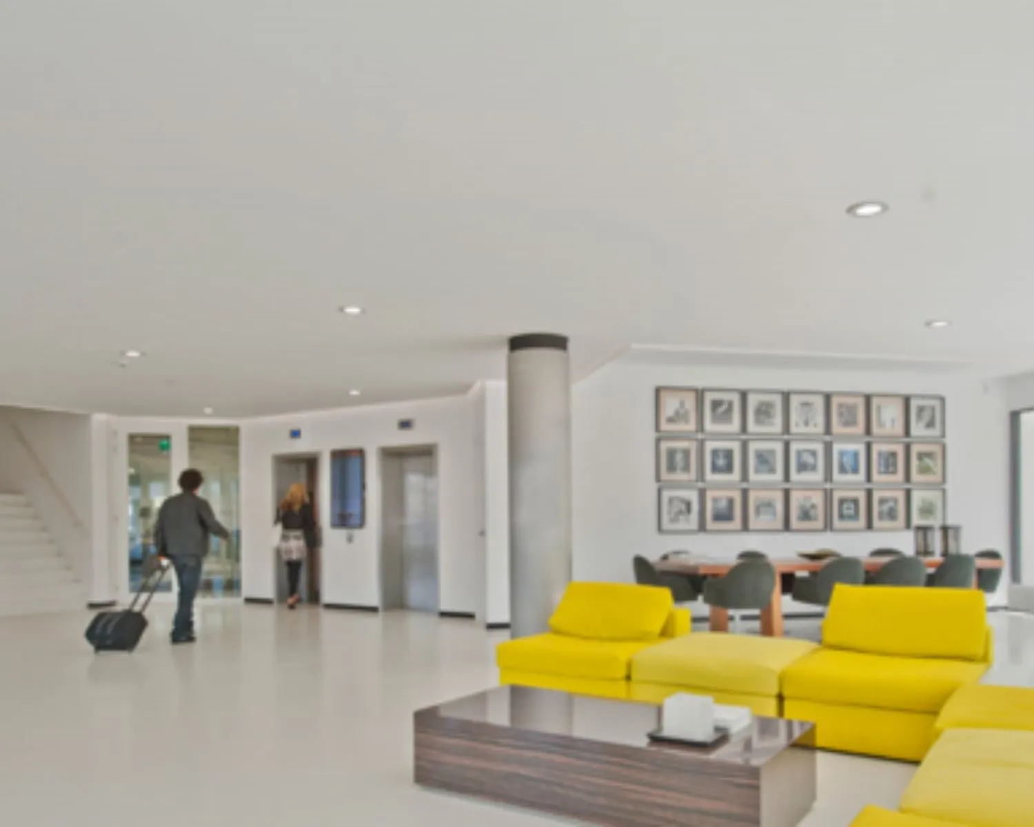 Moderne hotel lobby met gele zitbanken, een kunstmuur en mensen bij de lift.