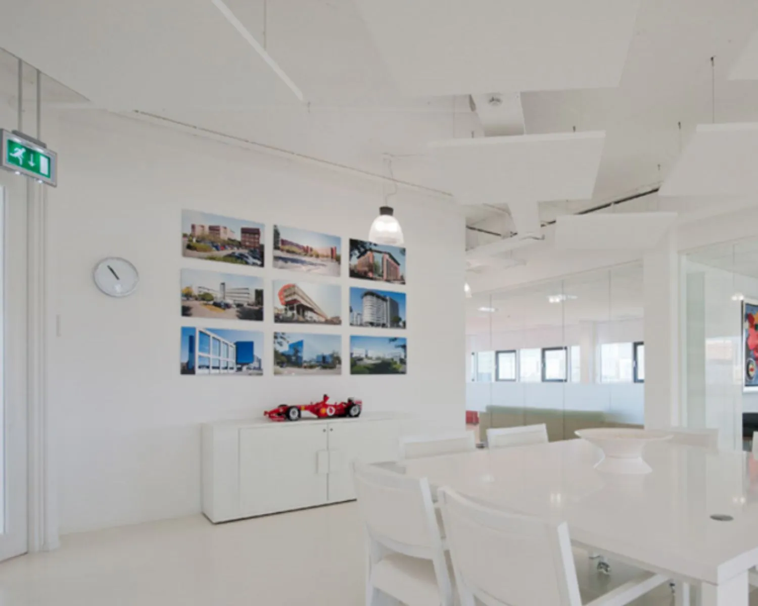 Moderne vergaderruimte met witte meubels, een wand met architectuurfoto's en een miniatuur raceauto op een kast.