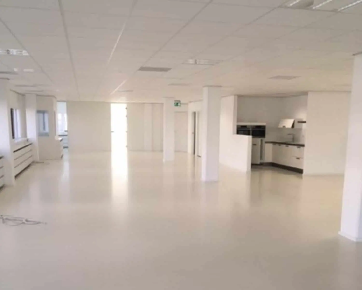 Lichte, lege kantoorruimte met ingebouwde keuken en witte vloer.