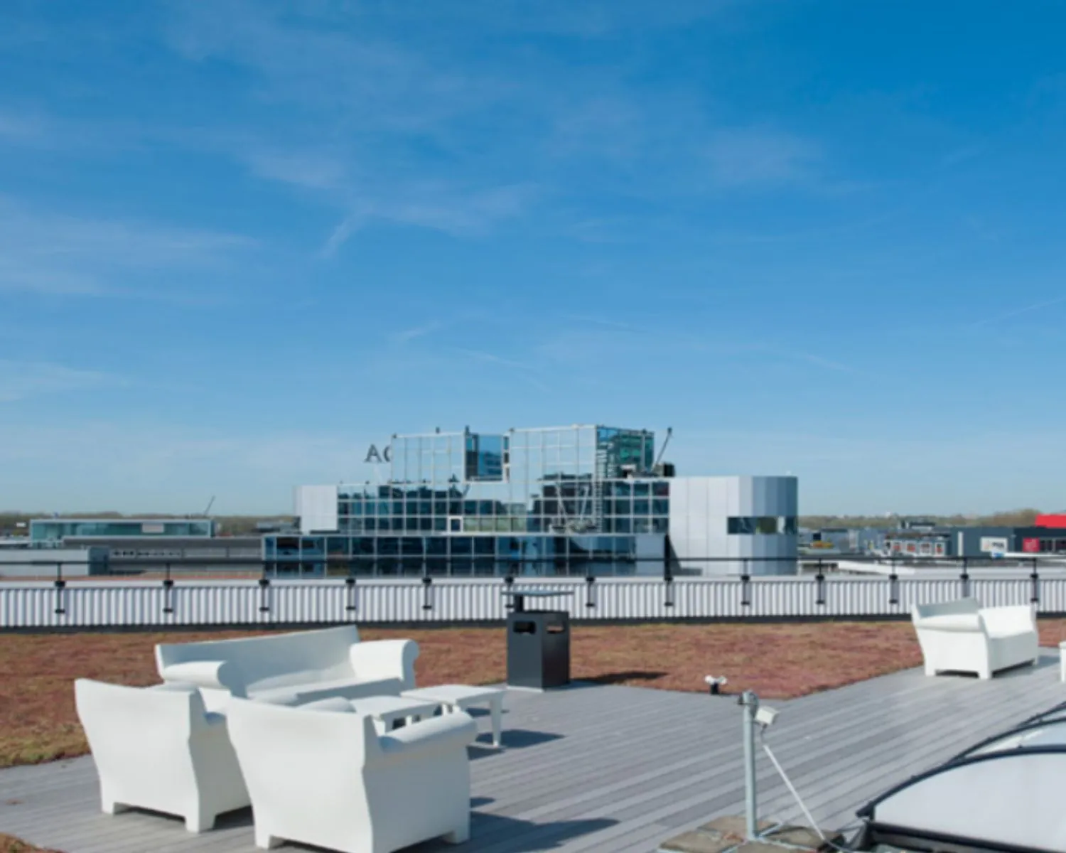 Dakterras met witte loungeset en uitzicht op een modern kantoorgebouw met spiegelende ramen.