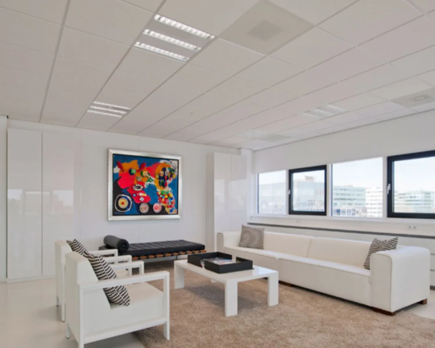 Modern ingerichte, lichte kantoorruimte met witte meubels, een beige vloerkleed en een kleurrijk kunstwerk aan de muur.