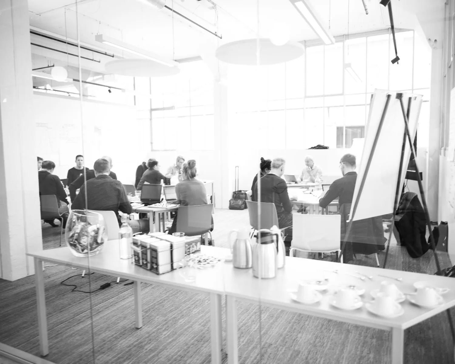 Een groep mensen zit in een vergaderruimte tijdens een zakelijke bijeenkomst, gezien door een glazen wand.