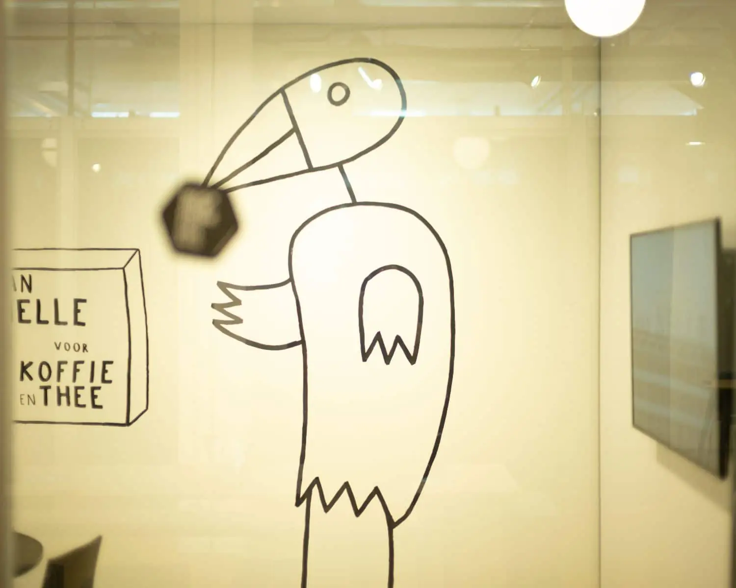 Zwart-witte muurtekening van een vogelachtig figuur met naast zich een doos waarop "voor koffie en thee" staat.