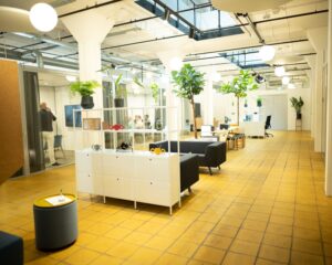 Modern ingerichte kantoortuin met glazen vergaderruimte, gele tegelvloer, planten en loungemeubilair.