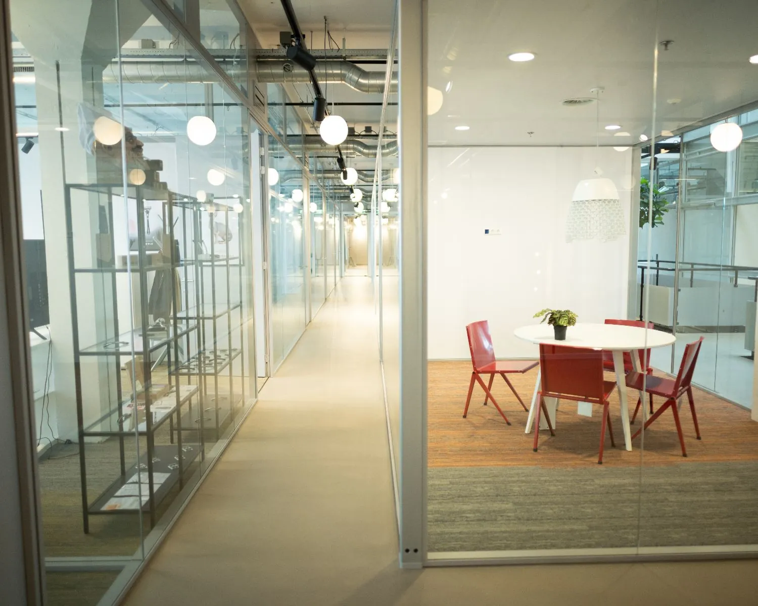 Vergaderruimte met ronde tafel en vier rode stoelen in een modern kantoor met glazen wanden.