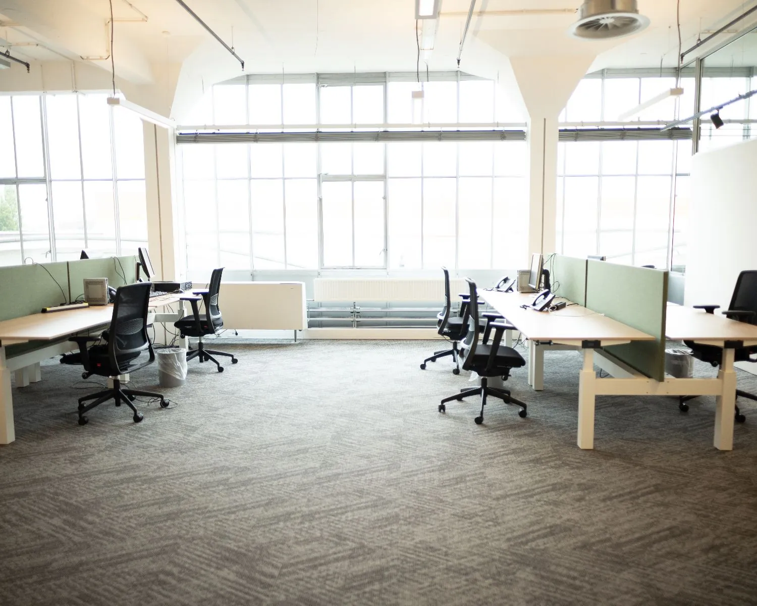 Een modern, licht open kantoor met meerdere bureaus, bureaustoelen en groene scheidingswanden.