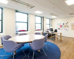 Moderne kantoorkamer met een vergadertafel, zes stoelen, een bureau en een prikbord aan de muur.