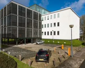 Modern kantoorgebouw met parkeergarage en slagboom op een zonnige dag.