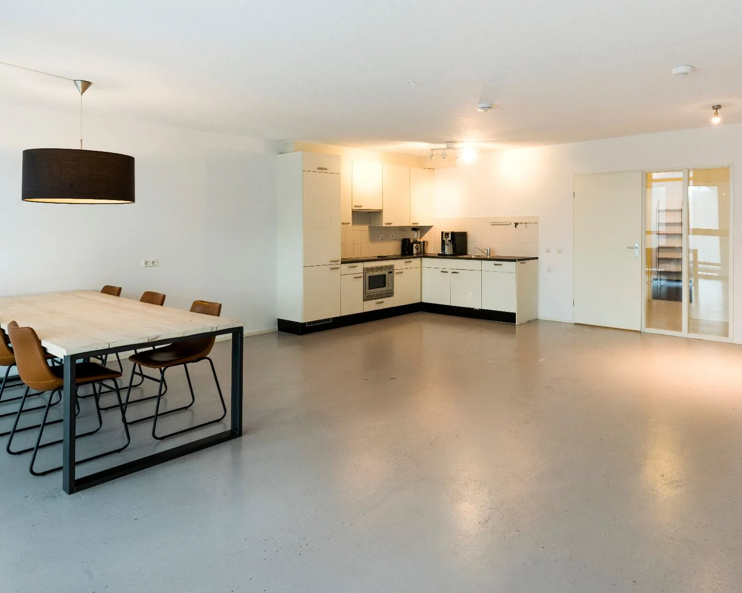 Moderne, minimalistisch ingerichte open keuken met eettafel en zes stoelen in een ruime, lichte kamer.