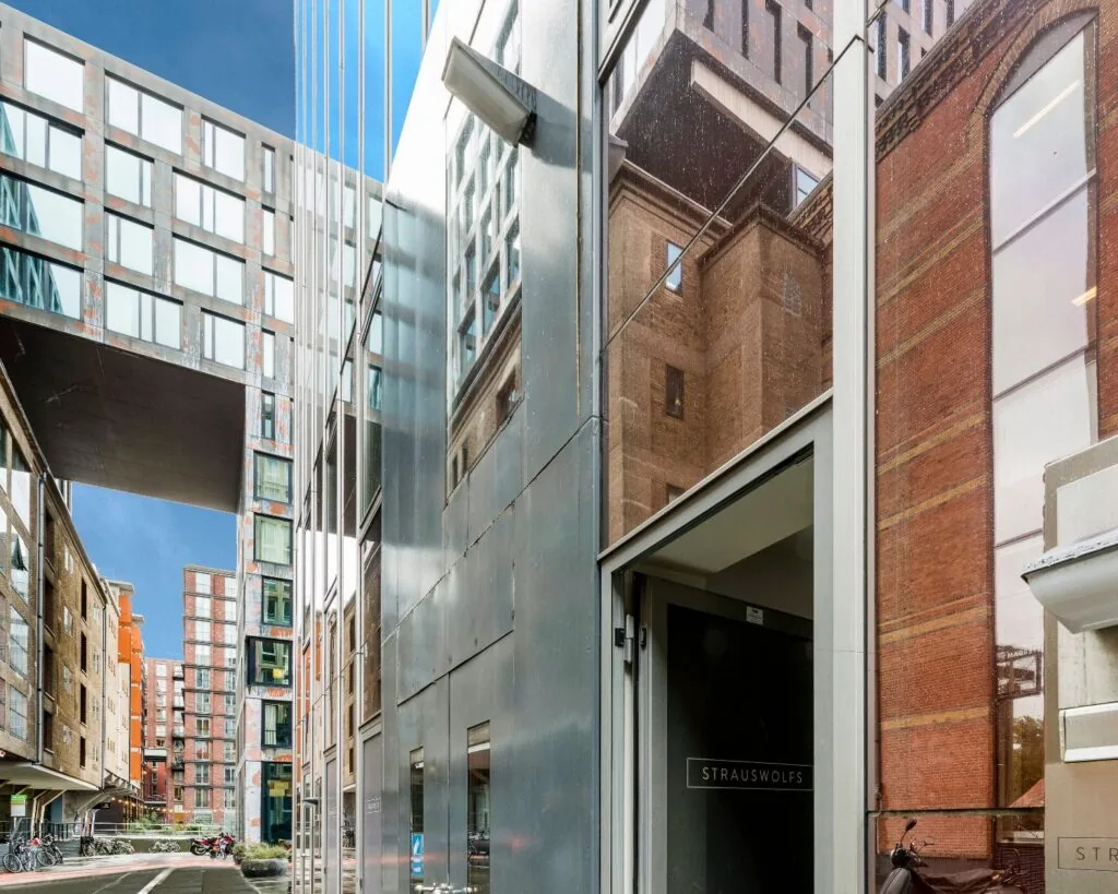Moderne straat met hoge gebouwen van glas en baksteen, met de ingang van het kantoorpand StrausWolfs op de voorgrond.
