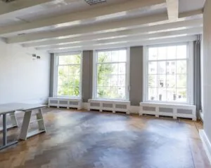 Lichte, lege kantoorruimte met houten visgraatvloer en grote ramen die uitkijken op een stadsomgeving.