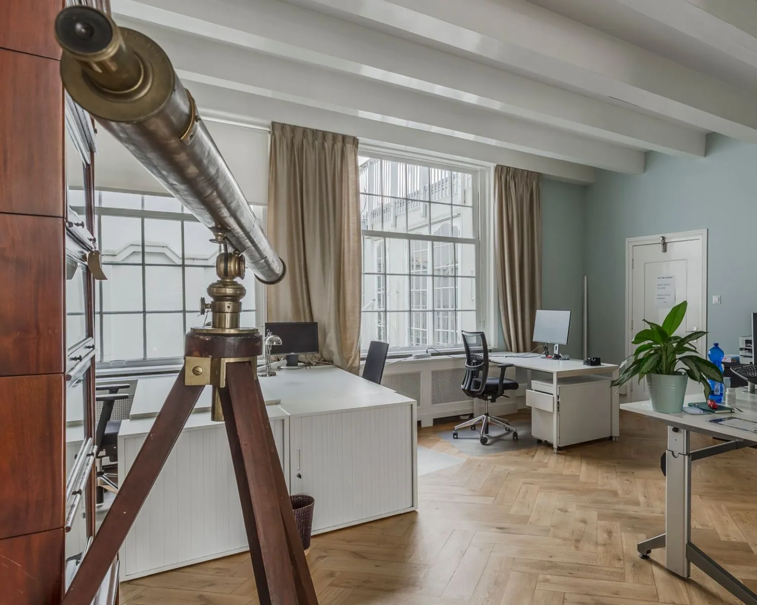Licht en modern kantoor met een antieke telescoop op een statief op de voorgrond.