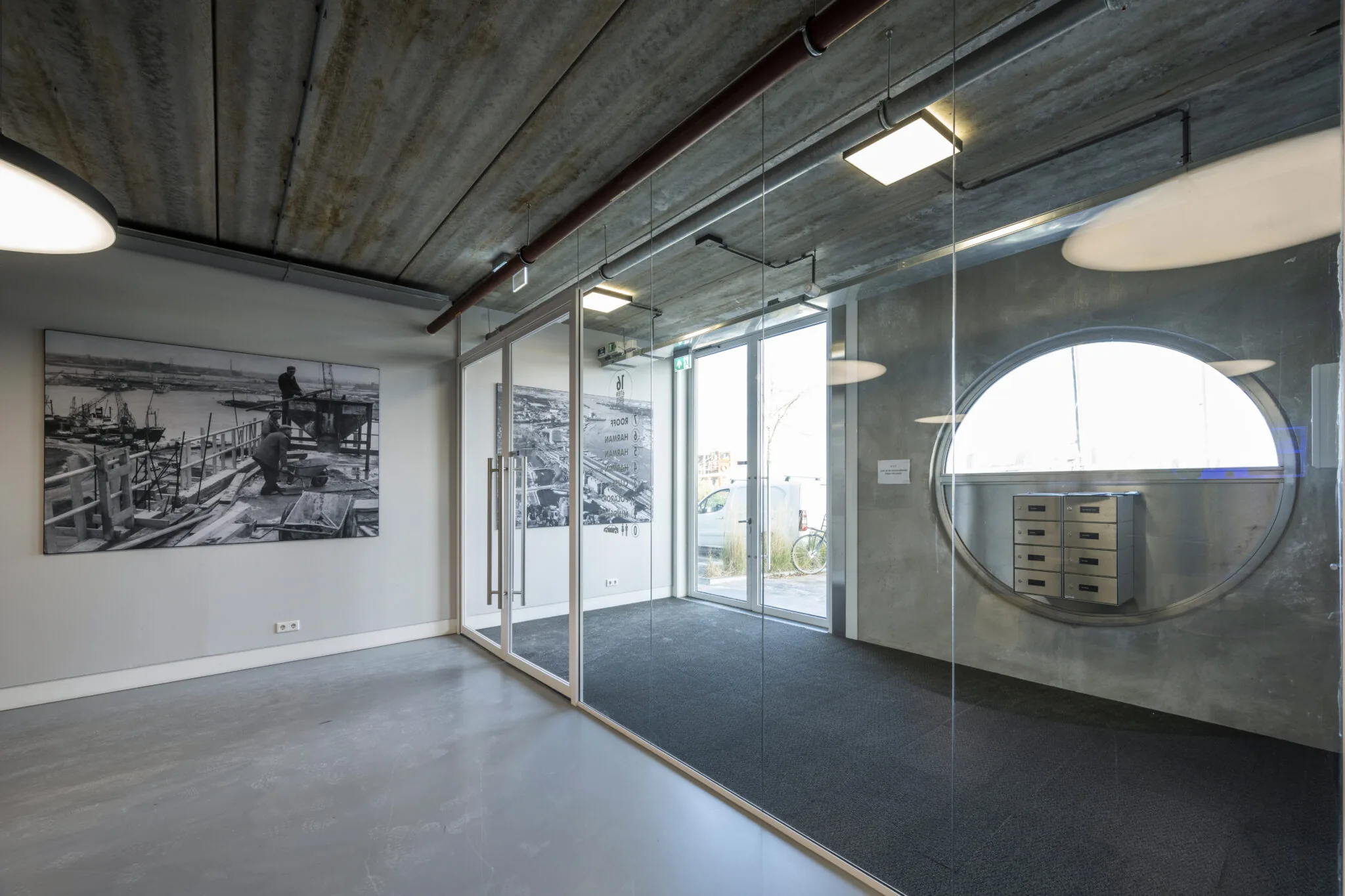 Moderne kantoorruimte aan de Danzigerkade met betonnen plafond, glazen wanden en zwart-witfoto’s van havenbouw door Paul Starink.