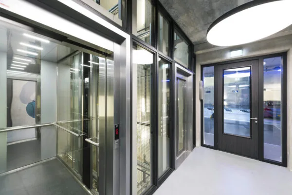 Moderne lifthal met glazen liften en betonnen plafond in gebouw aan de Danzigerkade, ontworpen door Paul Starink.