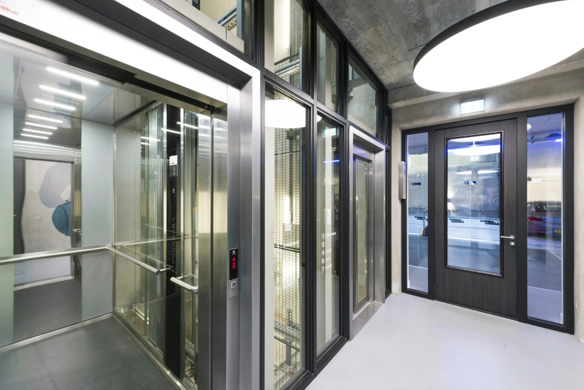 Moderne lifthal met glazen liften en betonnen plafond in gebouw aan de Danzigerkade, ontworpen door Paul Starink.