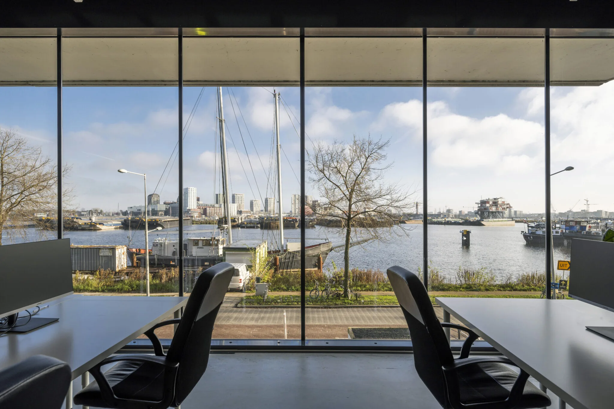 Uitzicht vanuit een modern kantoor aan de Danzigerkade op het IJ met boten, havengebied en de skyline van Amsterdam.